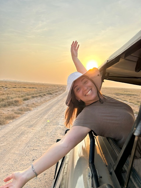 Female trip leader smiling while leaning out the window of a safari van in Africa