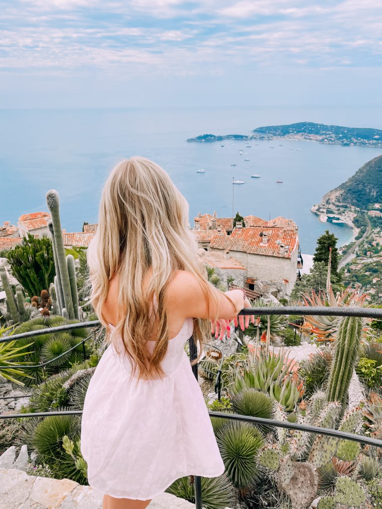 girl in a pink mini dress faces away from the camera overlooking the French coastline from the city of Eze