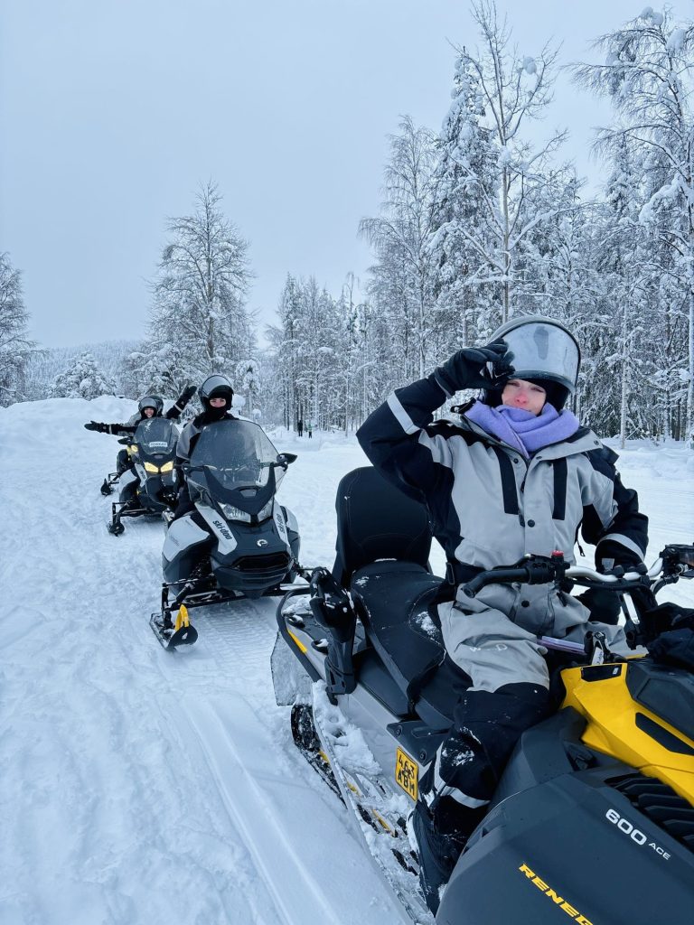 three girls pose on snowmobiles in the arctic forest of Lapland