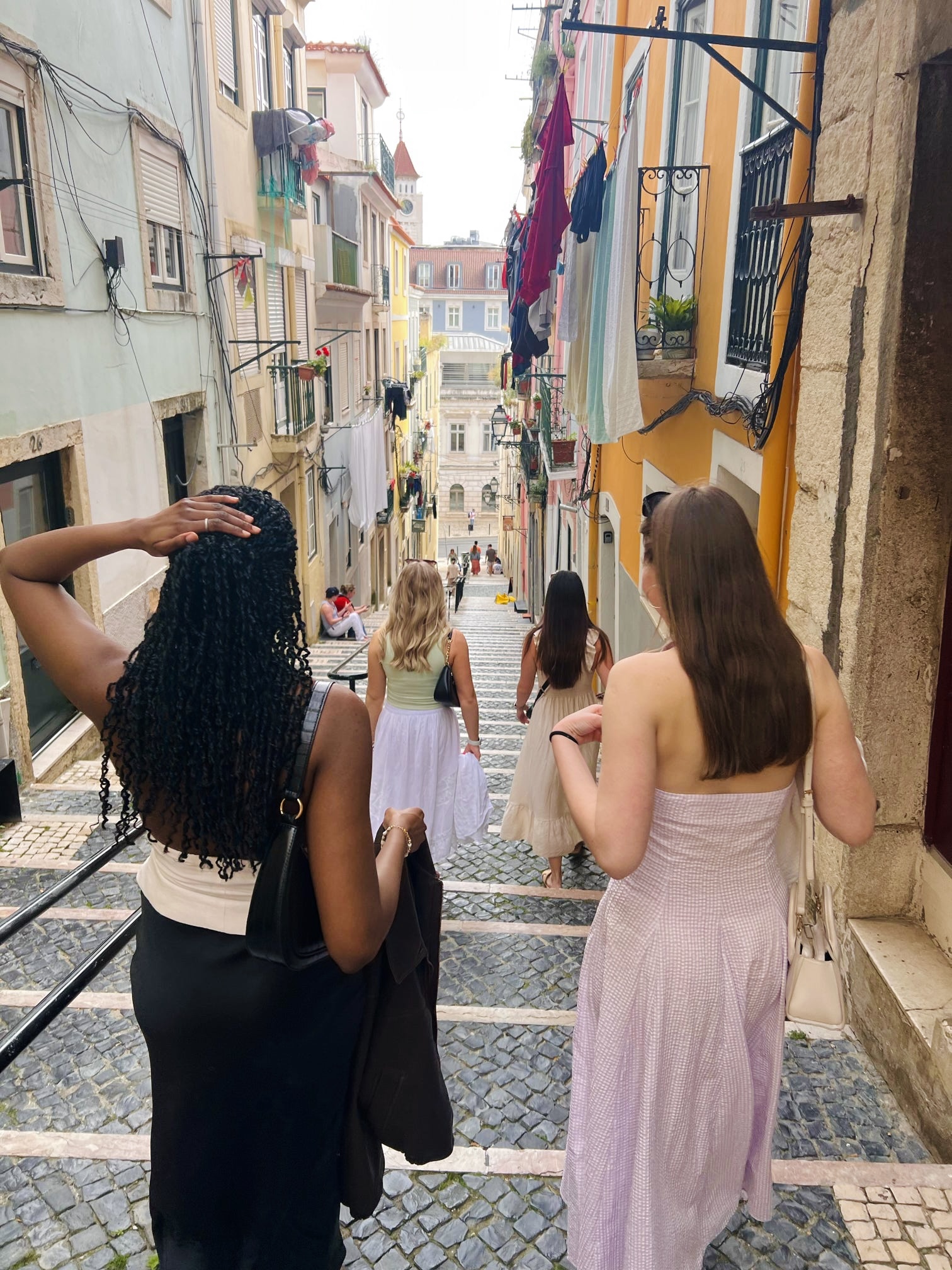 four girls in dresses walk in front of the camera heading down the steps on a street in Lisbon, Portugal