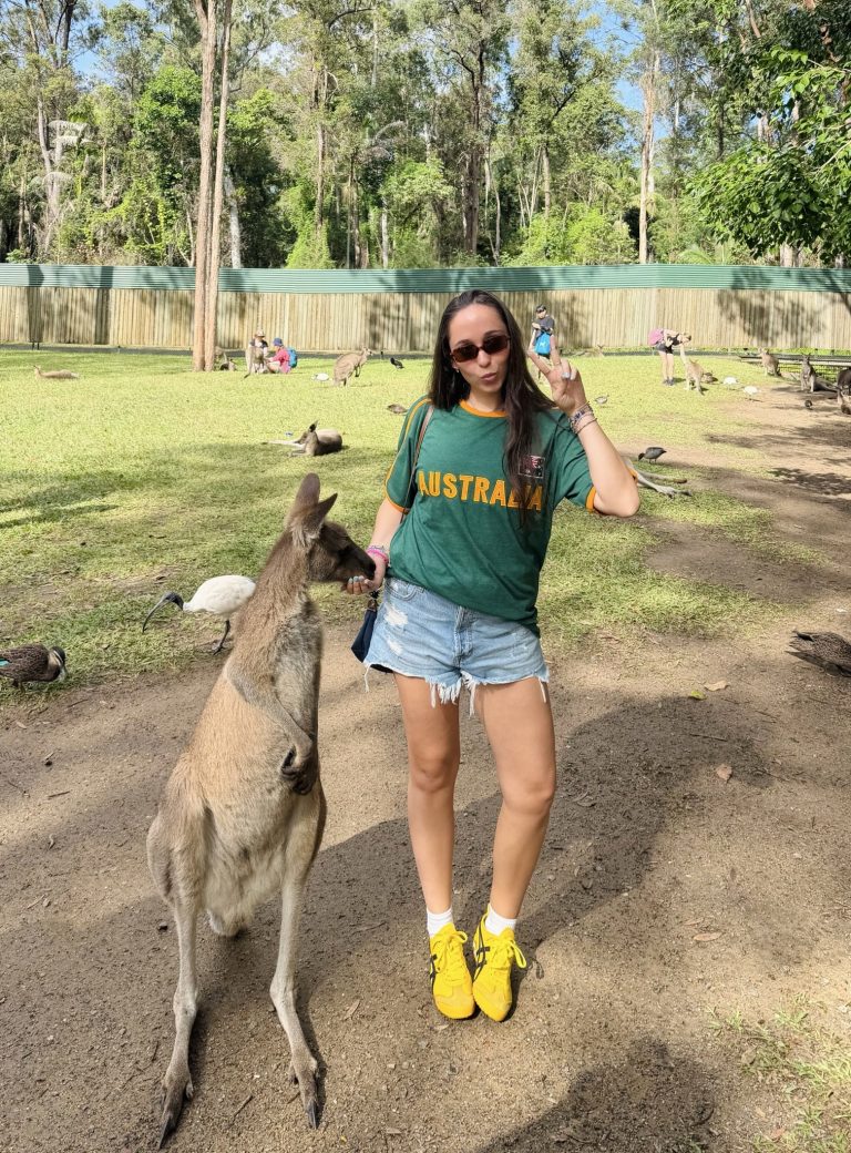 Young woman holds up a peace sign as she feeds a kangaroo at the Australia Zoo