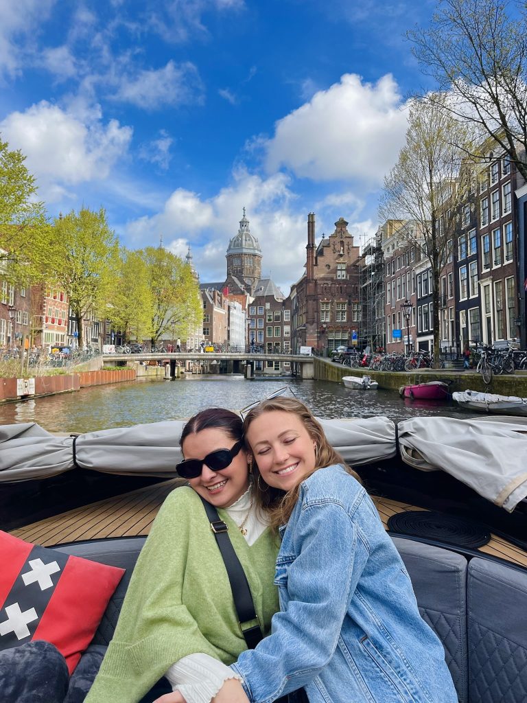 two girls hug in the back of a boat cruising down the canals of Amsterdam