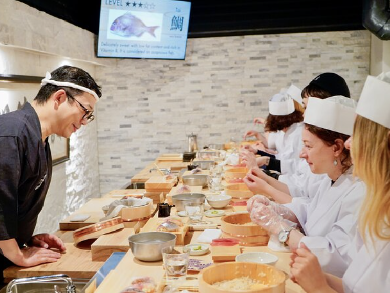 A sushi class with participants in white chef's hats and an instructor
